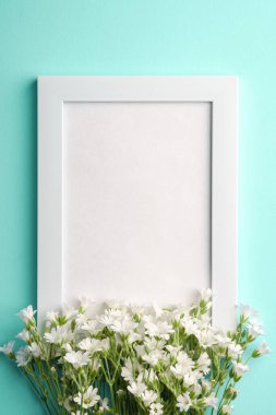 Mavi arkaplanda fare kulaklı civciv çiçekleri olan beyaz boş fotoğraf çerçevesi, üst görünüm kopyalama alanı