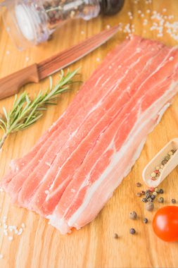 Çiğ pastırma şeritleri, tahtanın üzerinde. Bıçak, baharat, domates, biber değirmeni, tuz, sarımsak, biberiye.