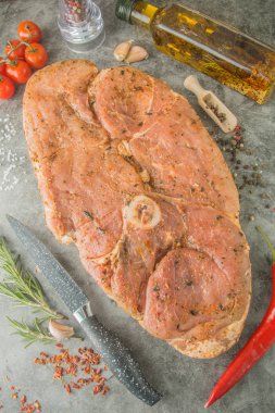 Ortasında yuvarlak kemik olan çiğ biftek, salamurada büyük bir parça, bıçak, baharatlar, üst manzara..