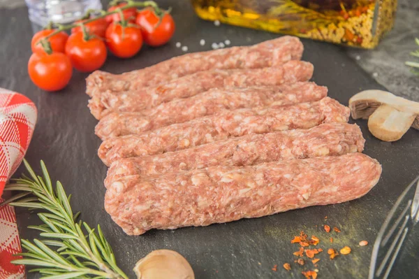 Mititei - Romanian sausages. Raw sausages with spices on a black slate. Close-up.