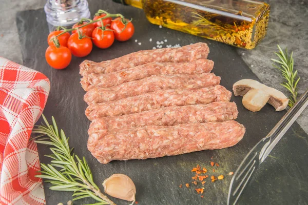Mititei - Romanian sausages. Raw sausages with spices on a black slate. Close-up.