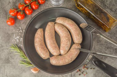 Mutfak maşasıyla tavada çiğ Münih sosisi. Üst görünüm.