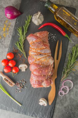 Siyah tahtada sicimle kaplı büyük bir parça et, baharatlar ve et çatalı, üst manzara.