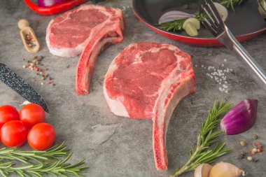 Pişirmeden önce iki çiğ baltalı biftek, tava ve baharatlı, yakın plan.