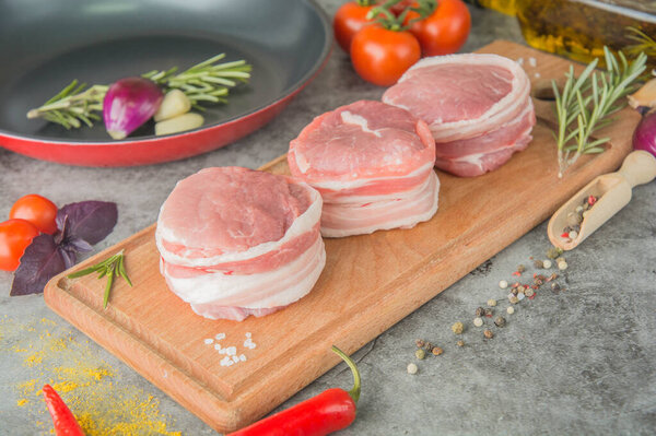 Three raw filet Mignon on a wooden board with spices, next to the pan, before cooking, side view