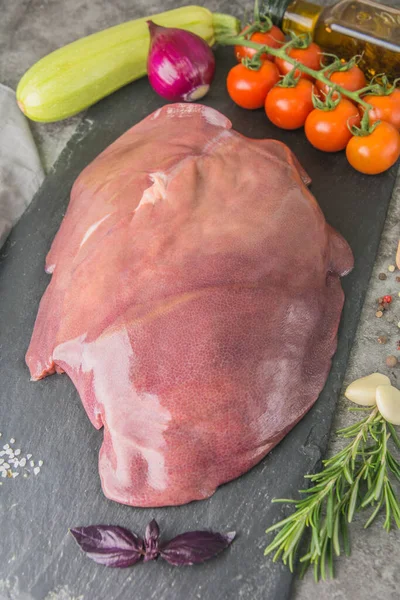 Kasap dükkanında baharat ve baharatlarla siyah tahtada büyük bir parça çiğ domuz ciğeri.
