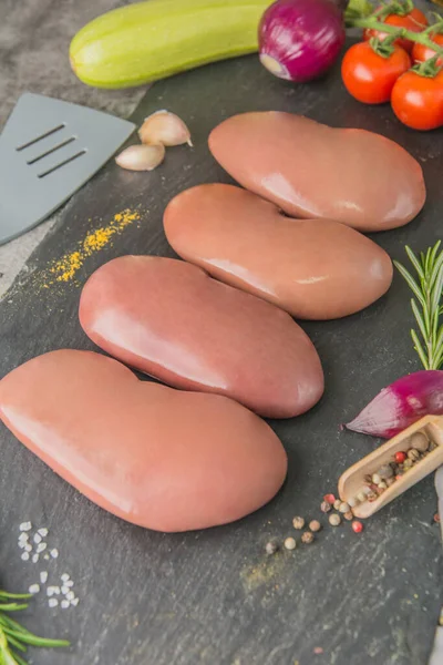 Raw pork kidneys on black slate with spices and seasonings in a butcher's shop, side view — Stock Image Raw Pork Kidneys Black Slate Spices Seasonings Butcher Shop Side Stock Photo
