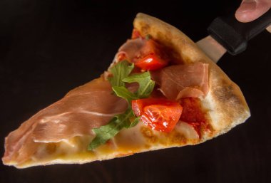 Bir dilim jambonlu pizza. Arka planda bulanık siyah bir arka plan. Pizza spatulasında yakın plan pizza..