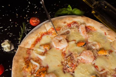 Karidesli pizza, pizza makasıyla kesilir. Siyah bir tabloda en üstteki görünüm.