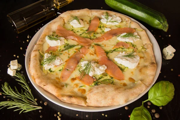 Ricotta pizzası, somon, çeşitli peynir ve otlarla. İçinde baharatlar ve malzemeler olan siyah bir masanın üzerinde. Menü için fotoğraf.