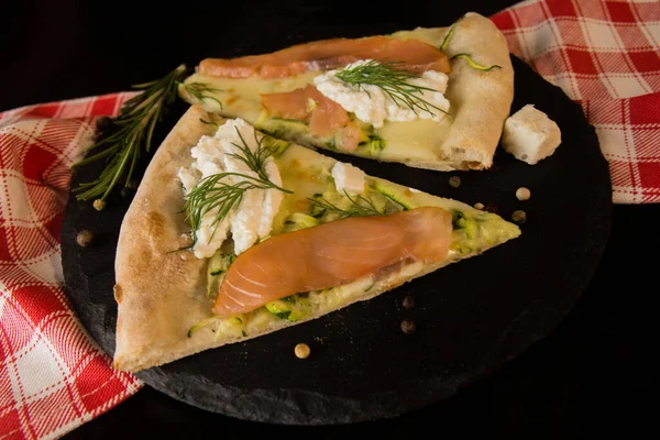 İki dilim somonlu pizza. Kırmızı kareli peçeteli siyah bir tahta üzerinde.