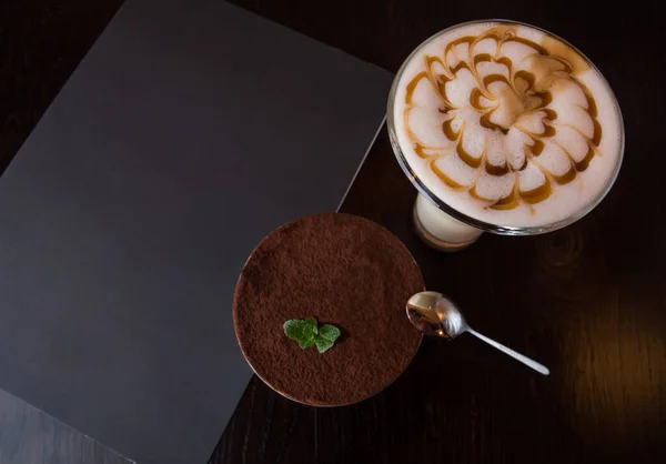 Tiramisu ve büyük bardakta kahve, üst manzara. Masada bir menü var..