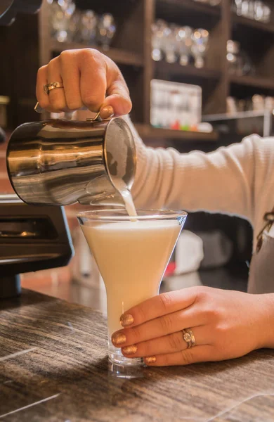 Latte yapmak - kadın elleri büyük bir bardağa sütlü kahve döker. Kafenin arkasında..