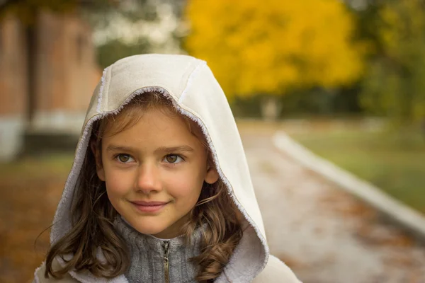 Brunette girl in a light coat with a hood in yellow autumn leave — Stock Photo, Image