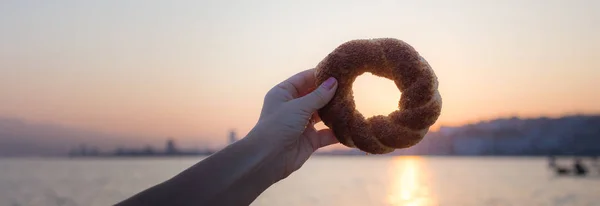 Τούρκικο bagel simit σε γυναίκες χέρι την αυγή με φόντο — Φωτογραφία Αρχείου