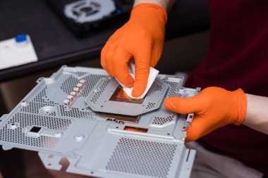 SAINT-PETERSBURG, RUSSIA, OCTOBER 27 2019: Men's hands in orange gloves cleans disassembled console PlayStation 4 Pro. Close-up, shallow depth of field