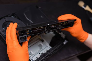SAINT-PETERSBURG, RUSSIA, OCTOBER 27 2019: Man in orange gloves parses the PlayStation 4 Pro console. Close-up, shallow depth of field
