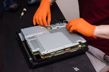 SAINT-PETERSBURG, RUSSIA, OCTOBER 27 2019: Man in orange gloves parses the PlayStation 4 Pro console. Close-up, shallow depth of field