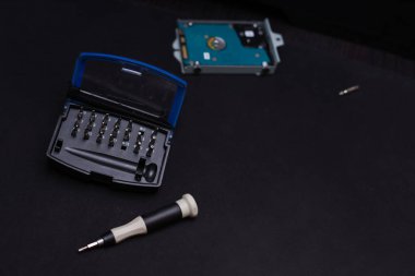 Elektronik aletler için tornavida ve enjektör seti siyah arka planda yatar. Yakınlarda bir sabit disk var, odak dışı. Yakın plan, yüzeysel alan derinliği, kopyalama alanı olan resim 
