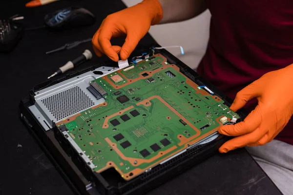 SAINT-PETERSBURG, RUSSIA, OCTOBER 27 2019: Man in orange gloves parses the PlayStation 4 Pro console. Close-up, shallow depth of field