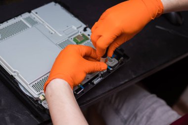 SAINT-PETERSBURG, RUSSIA, OCTOBER 27 2019: Man in orange gloves parses the PlayStation 4 Pro console with a screwdriver. Close-up, shallow depth of field