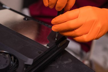 SAINT-PETERSBURG, RUSSIA, OCTOBER 27 2019: Man in orange gloves parses the PlayStation 4 Pro console with a screwdriver. Close-up, shallow depth of field