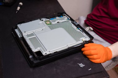 SAINT-PETERSBURG, RUSSIA, OCTOBER 27 2019: Man in orange gloves parses the PlayStation 4 Pro console with a screwdriver. Close-up, shallow depth of field