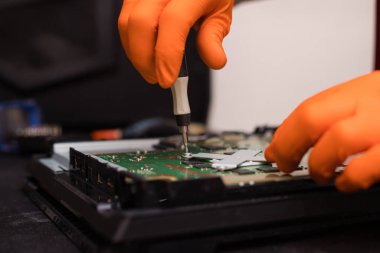 SAINT-PETERSBURG, RUSSIA, OCTOBER 27 2019: Man in orange gloves parses the PlayStation 4 Pro console with a screwdriver. Close-up, shallow depth of field