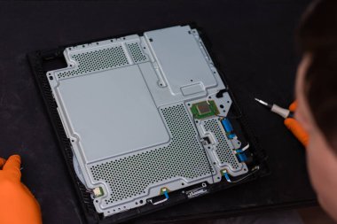 SAINT-PETERSBURG, RUSSIA, OCTOBER 27 2019: Man in orange gloves parses the PlayStation 4 Pro console with a screwdriver. Close-up, shallow depth of field