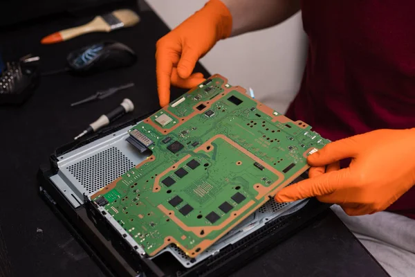 SAINT-PETERSBURG, RUSSIA, OCTOBER 27 2019: Man in orange gloves parses the PlayStation 4 Pro console. Close-up, shallow depth of field