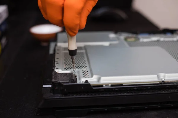 SAINT-PETERSBURG, RUSSIA, OCTOBER 27 2019: Man in orange gloves parses the PlayStation 4 Pro console with a screwdriver. Close-up, shallow depth of field