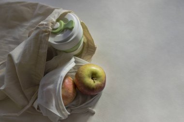 Güneş ışığının altında, üzerinde katlanabilir silikon bardak ve elmalar olan beyaz arka planda, yeniden kullanılabilir ağ torbası olan alışveriş torbası. Moda çevre dostu yeniden kullanılabilir şeyler kavramı. Boşluğu kopyala