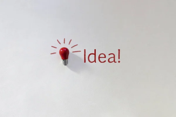 Small red light bulb top view on white background. Chalk inscription Idea. Concept thought arising. Top view picture with copy space