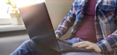 Dizüstü bilgisayarı olan kareli gömlek giyen bir adam evde çalışıyor. Pankart. Uzaktan kumanda. Online eğitim. Karantinaya alın. Kendini soyutlama. Serbest meslek hayatı.