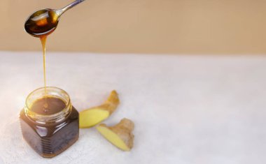 Karabuğday balı kaşıktan kavanoza dökülüyor ve yanında zencefil dilimi var. Doğal ilaçlar, sağlıklı yiyecekler, etnosbilim, bağışıklığın güçlendirilmesi. Metin için yer, yakın çekim, alanın sığ derinliği.