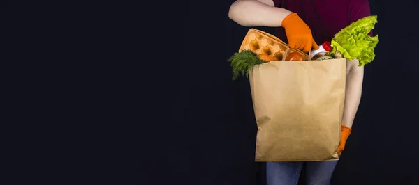 Covid-19 karantinası sırasında yemek teslimatı. Koruyucu eldiven giyen teslimatçı elinde yiyecek dolu kağıt torba tutuyor. Sebze, yumurta, yoğurt ve konserve yiyecekler. Yiyecek payları, gönüllü yardım.