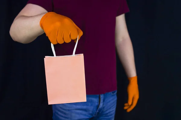 Gift delivery during quarantine of covid-19. Delivery man wearing protective gloves holds paper gift bag. Remote delivery of trifles