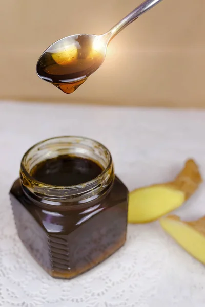 Buckwheat honey pours from spoon into jar and sliced ginger lying near. Natural medicine, healthy food, ethnoscience, strengthening immunity. Vertical picture, close-up, selective focus.