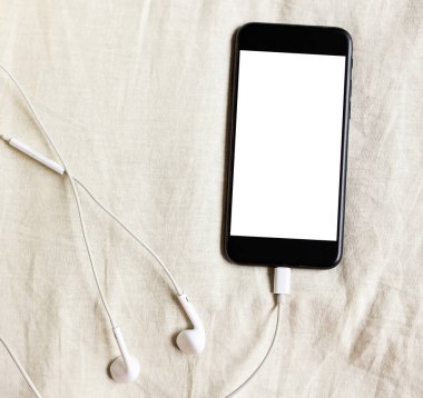 Kulaklık takan akıllı telefon, yatak manzarası buruşuk, alan derinliği sığ. Karantinaya alınırken evde kal. Mesafe öğrenme. Çevrimiçi çağrı. Uzaktan kumanda. Teletıp. Beyaz maket boş ekran. 