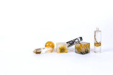 Beyaz arka planda epoksi reçineden yapılmış kristallerin içinde kurumuş çiçekleri olan kolyeler. Yakın çekim alan derinliği. El yapımı, DIY bijouterie düz yatıyordu