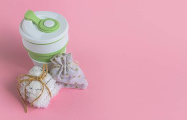 Katlanabilir silikon bardak, ağ torbası ve sicimle tutturulmuş yüz veya makyaj malzemesi için yeniden kullanılabilir pamuk diskler. Pembe arka planda sıfır atık kavramı telif alanı ile üst görünüm. Çevre dostu yaşam tarzı 