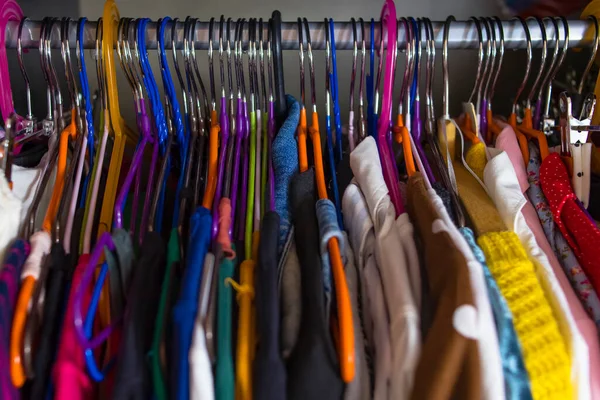 Women\'s wardrobe close-up shallow depth of field. Closet is tightly packed with clothes on multi-colored hangers. Disorganized wardrobe