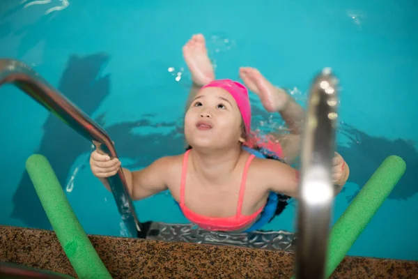 Pretty little girl learning to swim in the pool with swim coach trainer