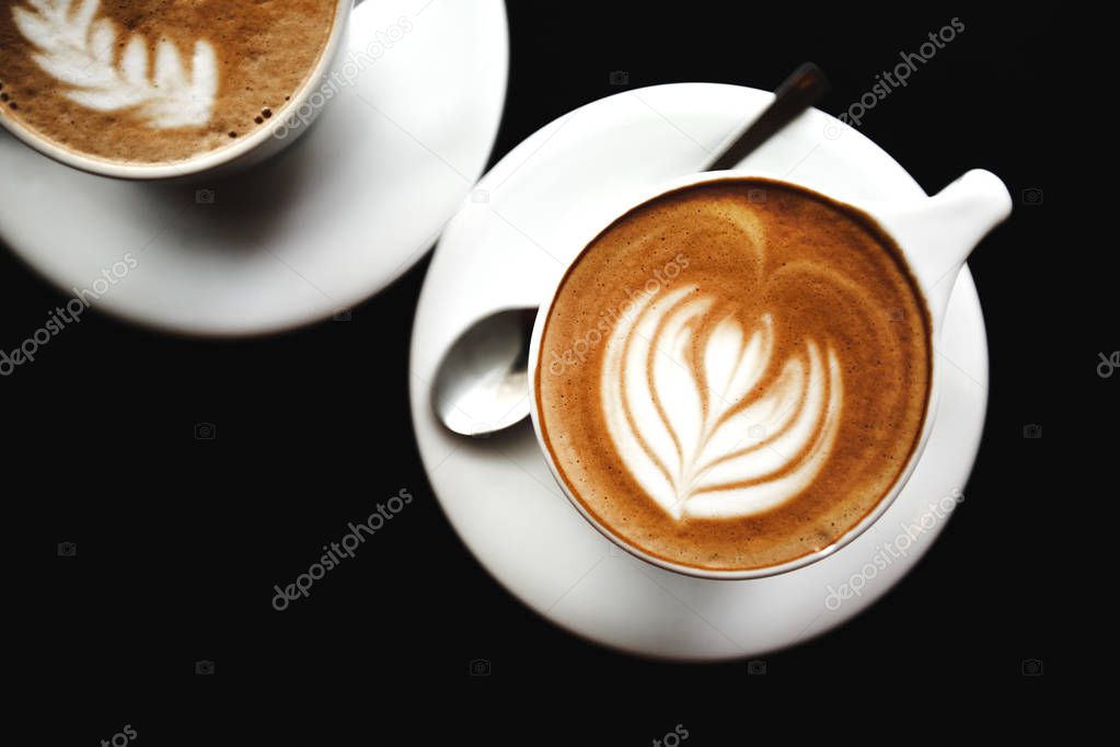 Two cups of cappuccino on black table