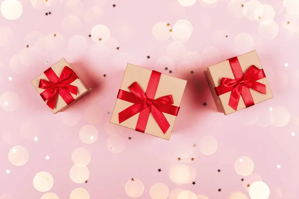 Three presents with red bow on pastel trendy pink background with little silver sparkles. Flat lay style. Christmas lights overlayed