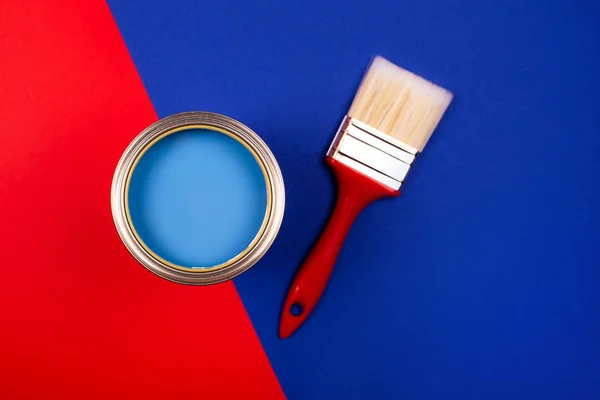 Penseel op open blik blauwe verf op blauwe en rode ondergrond. — Stockfoto