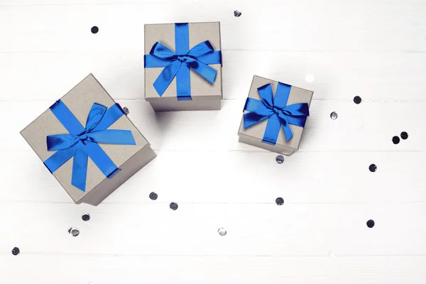 Three present boxes with blue bow on wooden background.