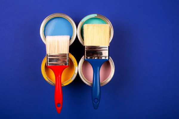 Four open cans of paint with brushes on bright background.