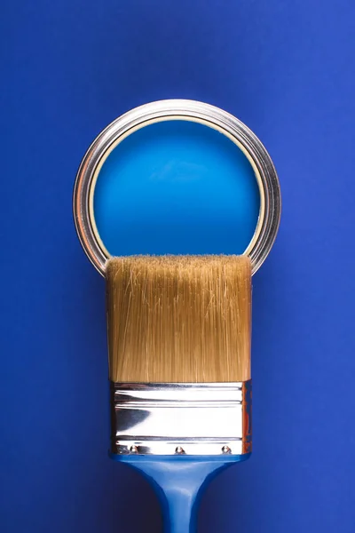 Brush on open can of blue paint on blue background. — Stock Photo, Image