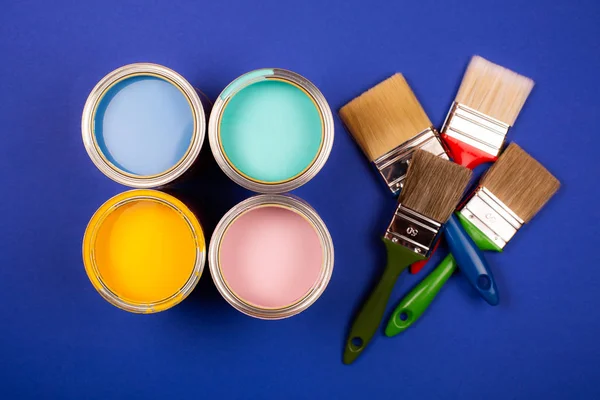 Cuatro latas abiertas de pintura con pinceles sobre fondo brillante . — Foto de Stock